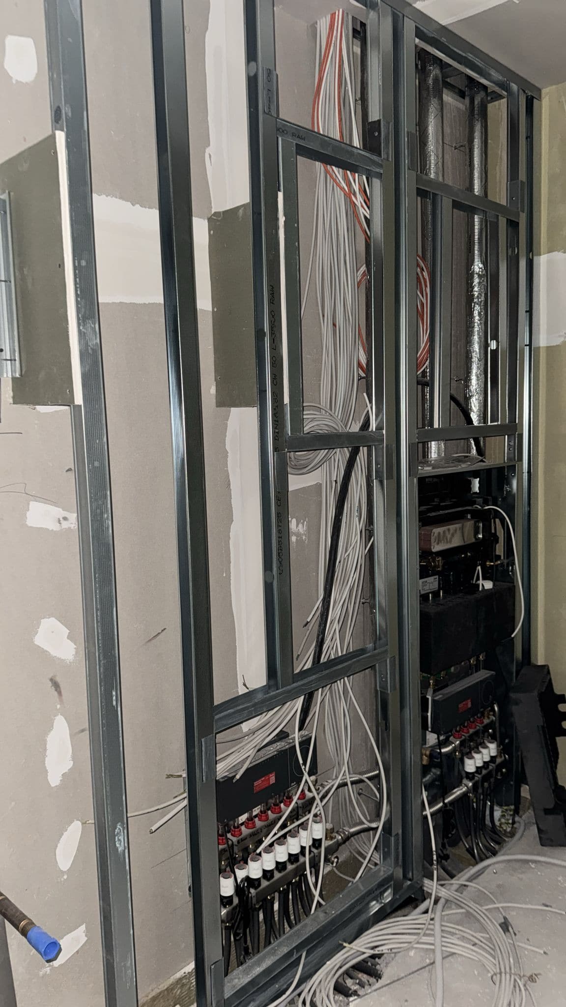 Installationsschacht mit zwei Heizkreisverteilern, gedämmter Lüftungsleitung und einem Bündel Elektroleitungen zwischen Metallständerprofilen